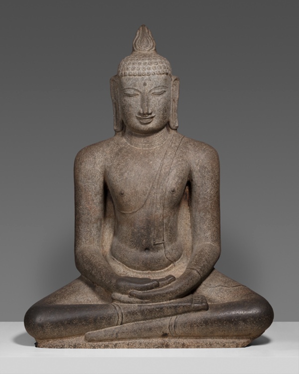 Dark stone sculpture of Buddha sitting cross-legged, hands in lap, eyes closed.